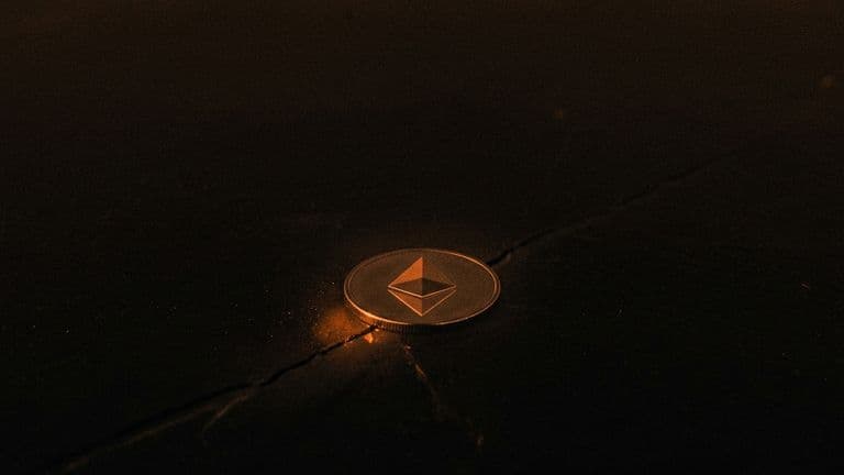 A coin with the Ethereum mark lies on a dark sheet of ice, with a thin crack spreading out from beneath it.