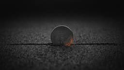 A coin with the Bitcoin mark stands upright in dark sand, resting exactly on a single straight line drawn across the sand, with darkness above.